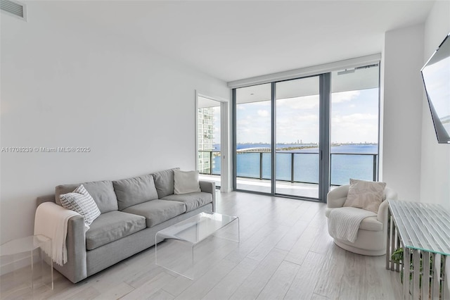 living area with floor to ceiling windows, visible vents, and light wood-type flooring