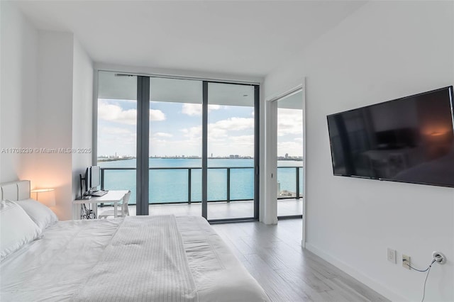 bedroom with access to exterior, wood finished floors, floor to ceiling windows, and baseboards