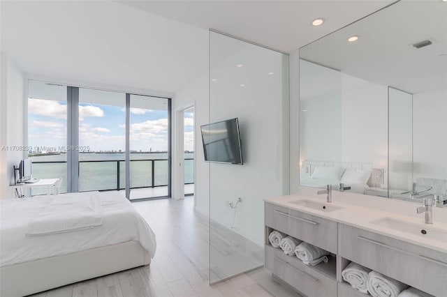 bedroom with access to outside, sink, light wood-type flooring, and a wall of windows