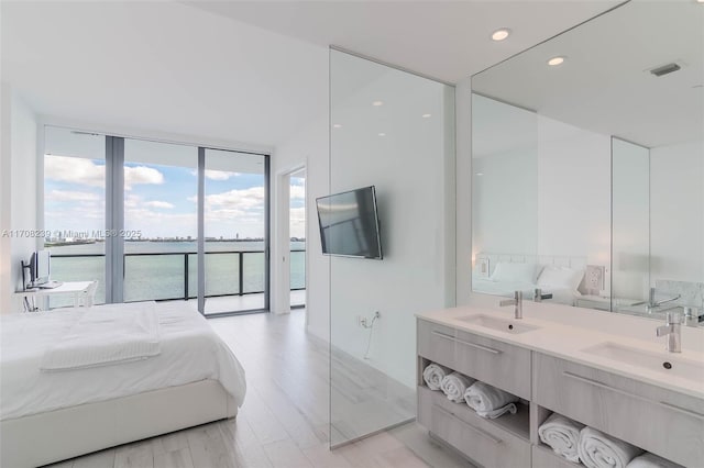 bedroom featuring expansive windows, visible vents, light wood-type flooring, and a sink