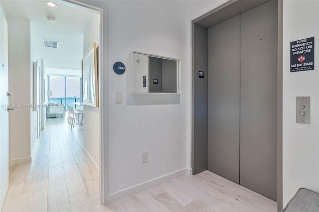 hallway with light wood finished floors, baseboards, visible vents, and elevator