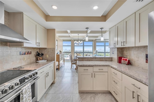 kitchen featuring wall chimney exhaust hood, stainless steel range, a raised ceiling, decorative light fixtures, and an inviting chandelier