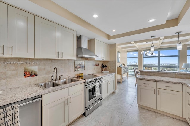 kitchen featuring wall chimney range hood, sink, light stone countertops, appliances with stainless steel finishes, and decorative light fixtures