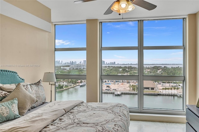 bedroom featuring ceiling fan, a water view, light tile patterned floors, and a wall of windows