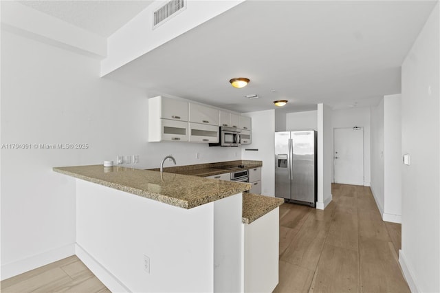 kitchen featuring white cabinets, appliances with stainless steel finishes, kitchen peninsula, and dark stone countertops