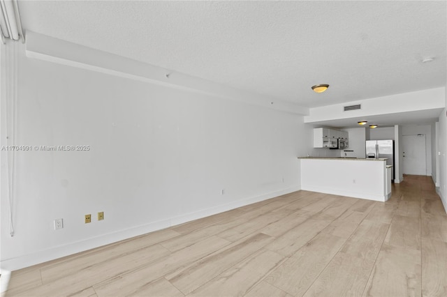 unfurnished living room featuring a textured ceiling and light wood-type flooring