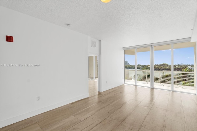 spare room with expansive windows, a textured ceiling, and light hardwood / wood-style flooring