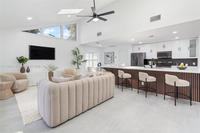 tiled living room with a skylight, ceiling fan, sink, and high vaulted ceiling