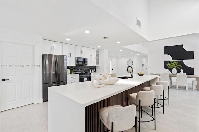 kitchen featuring backsplash, a breakfast bar, stainless steel appliances, a center island with sink, and white cabinetry