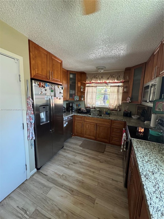 kitchen with light stone countertops, a textured ceiling, stainless steel appliances, and light hardwood / wood-style floors