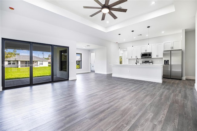 unfurnished living room with sink, ceiling fan, a raised ceiling, and dark wood-type flooring