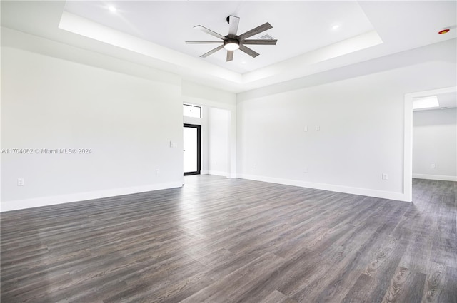 unfurnished room featuring a raised ceiling, ceiling fan, and dark hardwood / wood-style flooring