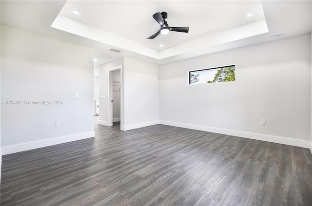 spare room with a tray ceiling, ceiling fan, and dark hardwood / wood-style flooring