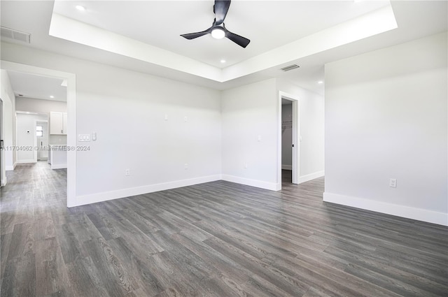 unfurnished room featuring dark hardwood / wood-style flooring, a tray ceiling, and ceiling fan