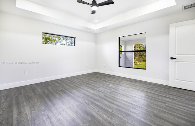 spare room featuring a raised ceiling, ceiling fan, and dark wood-type flooring