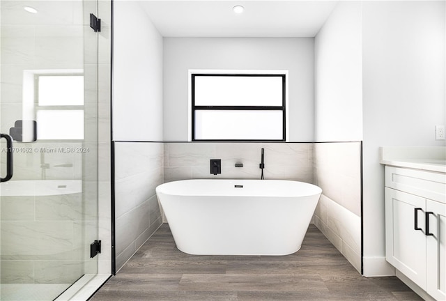 bathroom featuring plus walk in shower, hardwood / wood-style floors, vanity, and tile walls