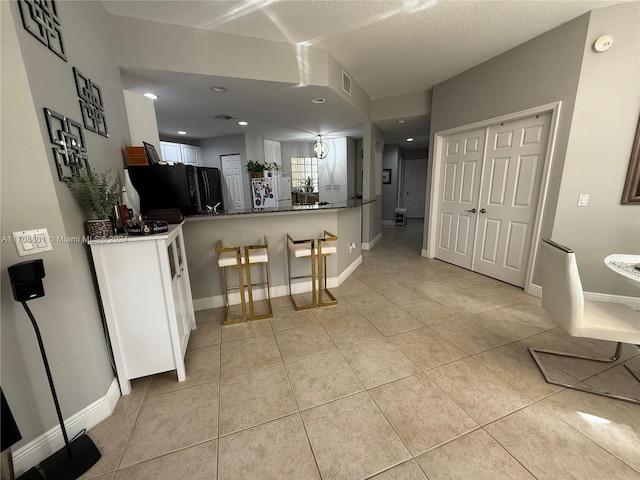 kitchen featuring black fridge, kitchen peninsula, white fridge, a textured ceiling, and light tile patterned flooring