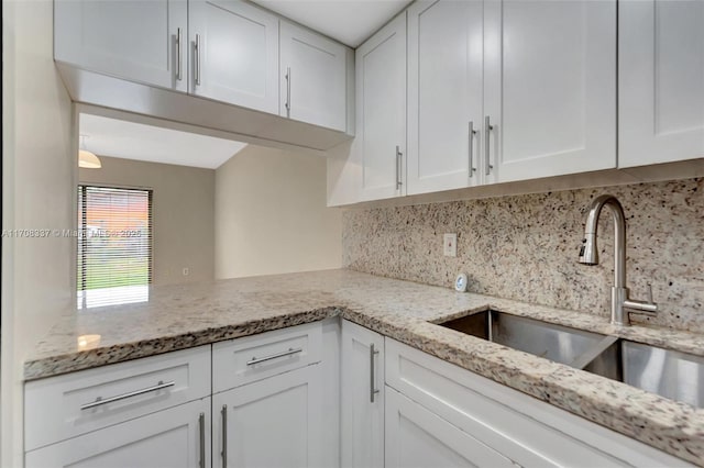 kitchen featuring light stone counters, a sink, and white cabinetry