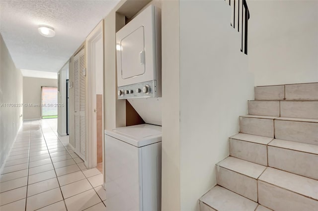 clothes washing area featuring a textured ceiling, laundry area, light tile patterned floors, and stacked washer / drying machine