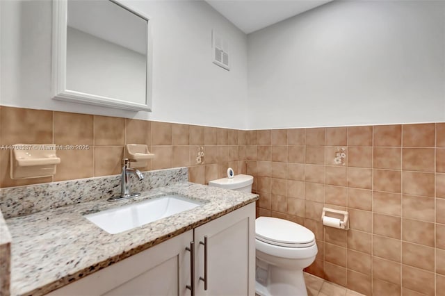 bathroom with toilet, visible vents, tile walls, and vanity