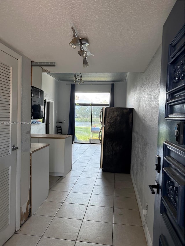 kitchen with light tile patterned floors, baseboards, a textured wall, freestanding refrigerator, and a textured ceiling