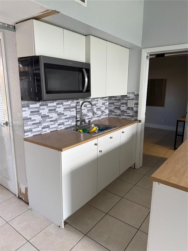 kitchen with tasteful backsplash, stainless steel microwave, light tile patterned flooring, and a sink