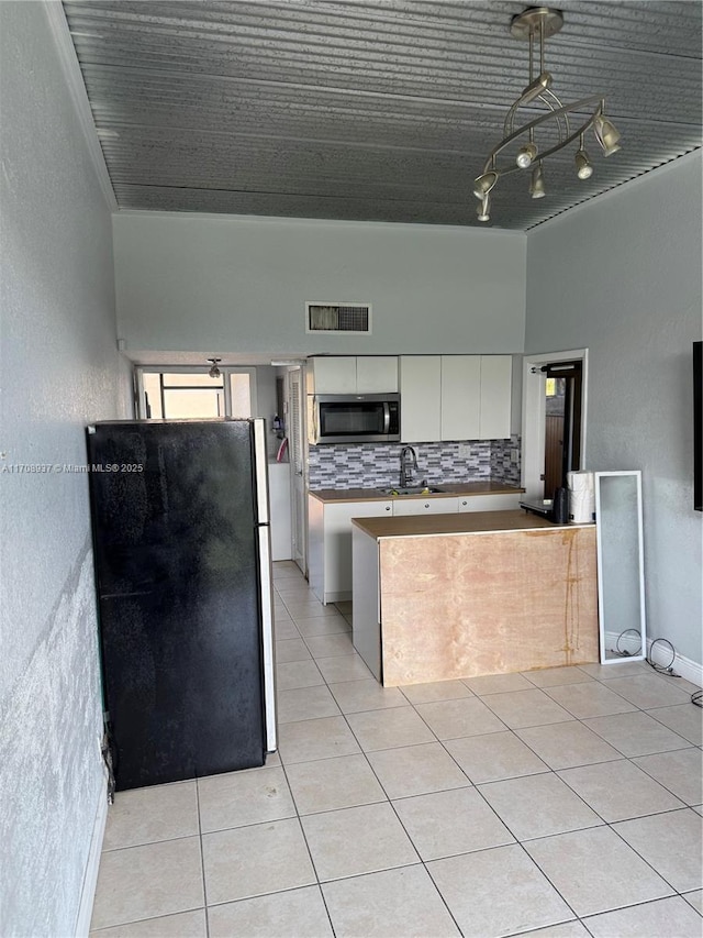 kitchen featuring light tile patterned floors, visible vents, white cabinets, freestanding refrigerator, and stainless steel microwave