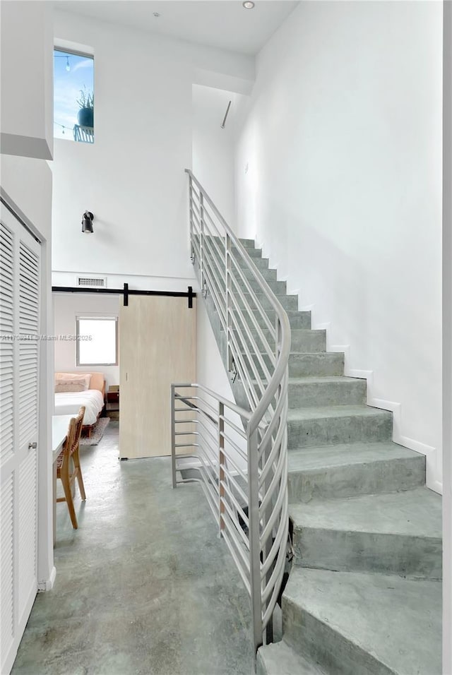 stairs featuring concrete flooring, a high ceiling, and a barn door