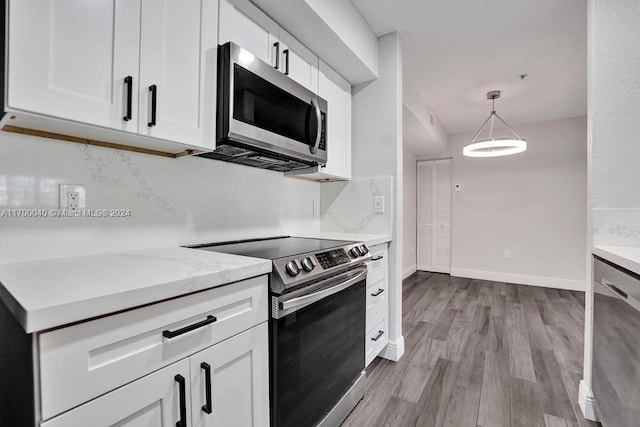 kitchen featuring light stone counters, stainless steel appliances, pendant lighting, white cabinets, and light hardwood / wood-style floors