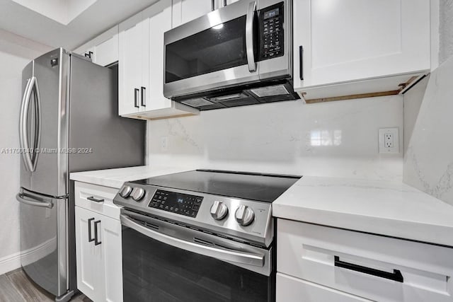 kitchen with hardwood / wood-style floors, backsplash, white cabinets, light stone countertops, and stainless steel appliances