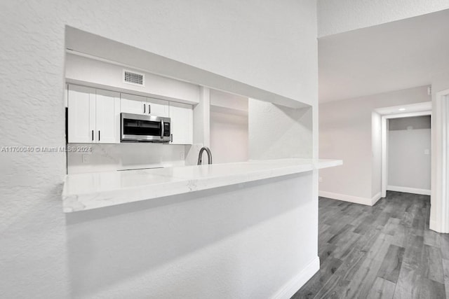 kitchen with white cabinetry, sink, light stone countertops, kitchen peninsula, and hardwood / wood-style flooring