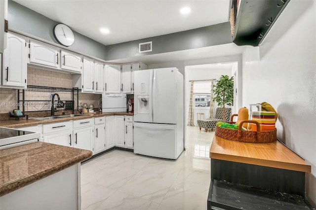 kitchen featuring white refrigerator with ice dispenser, white cabinets, sink, decorative backsplash, and dark stone countertops