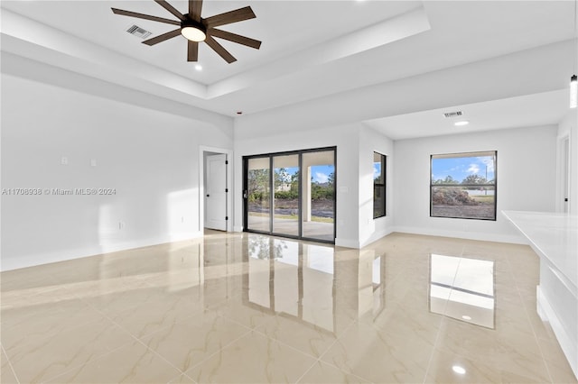 empty room with a raised ceiling, a wealth of natural light, and ceiling fan