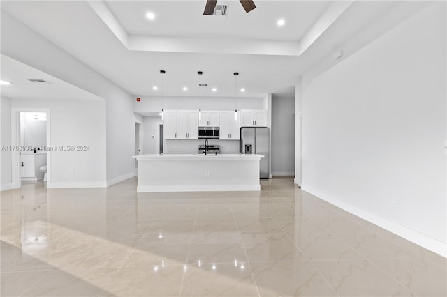 kitchen with white cabinetry, decorative light fixtures, a tray ceiling, a kitchen island with sink, and appliances with stainless steel finishes