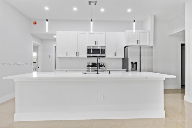 kitchen with a kitchen island with sink, pendant lighting, white cabinets, and stainless steel appliances