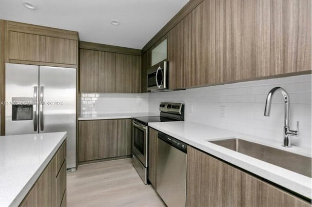 kitchen with backsplash, sink, light hardwood / wood-style floors, and appliances with stainless steel finishes