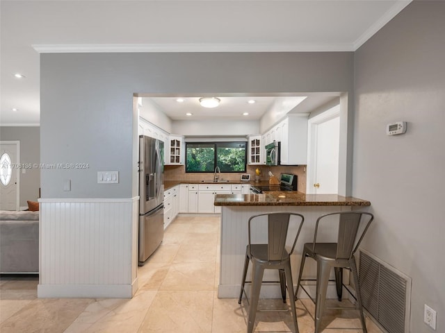 kitchen with kitchen peninsula, dark stone counters, stainless steel appliances, sink, and white cabinetry