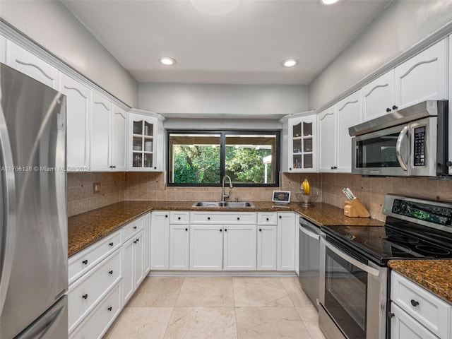 kitchen featuring decorative backsplash, dark stone counters, stainless steel appliances, sink, and white cabinetry