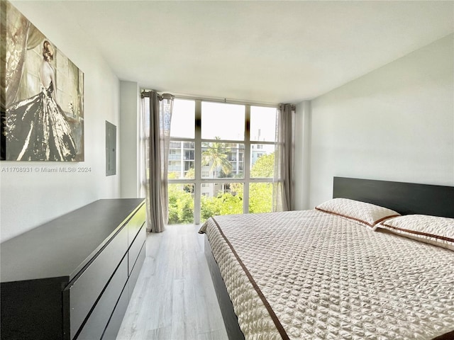 bedroom with electric panel, floor to ceiling windows, and light hardwood / wood-style floors