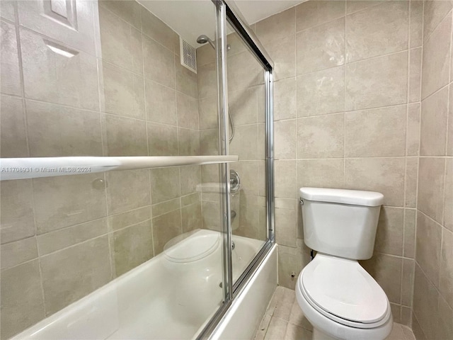 bathroom featuring tile patterned floors, toilet, bath / shower combo with glass door, and tile walls