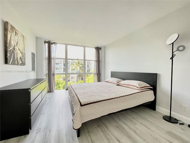 bedroom with electric panel, light hardwood / wood-style floors, and a wall of windows