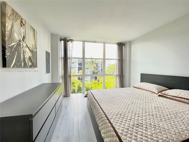 bedroom with floor to ceiling windows, electric panel, and light hardwood / wood-style flooring