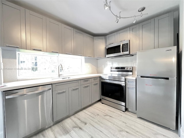 kitchen with gray cabinetry, sink, stainless steel appliances, tasteful backsplash, and light wood-type flooring