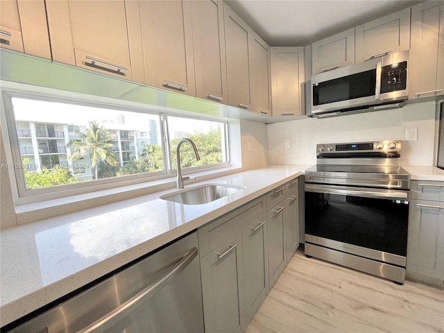 kitchen with light stone countertops, appliances with stainless steel finishes, gray cabinetry, sink, and light hardwood / wood-style flooring