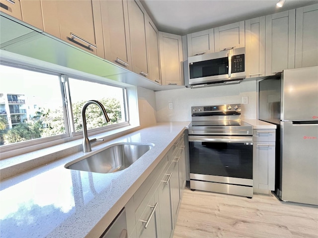 kitchen with appliances with stainless steel finishes, light stone counters, gray cabinetry, sink, and light hardwood / wood-style floors