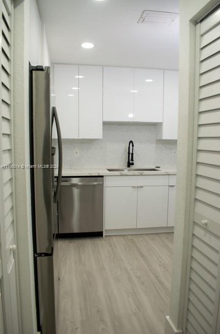 kitchen with sink, white cabinets, light wood-type flooring, and appliances with stainless steel finishes