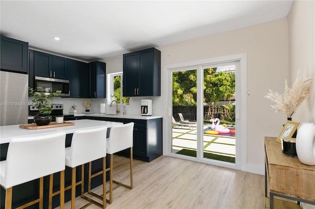 kitchen featuring sink, tasteful backsplash, light wood-type flooring, appliances with stainless steel finishes, and a kitchen breakfast bar