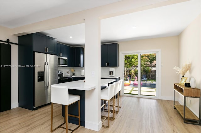 kitchen featuring a barn door, stainless steel appliances, a kitchen breakfast bar, and light wood-type flooring