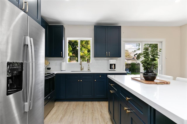 kitchen with sink, stainless steel fridge, decorative backsplash, light wood-type flooring, and electric stove