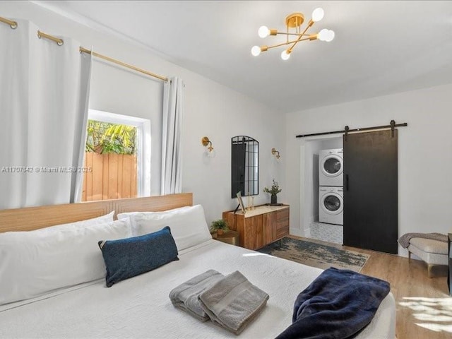 bedroom with a barn door, stacked washing maching and dryer, a chandelier, and hardwood / wood-style flooring